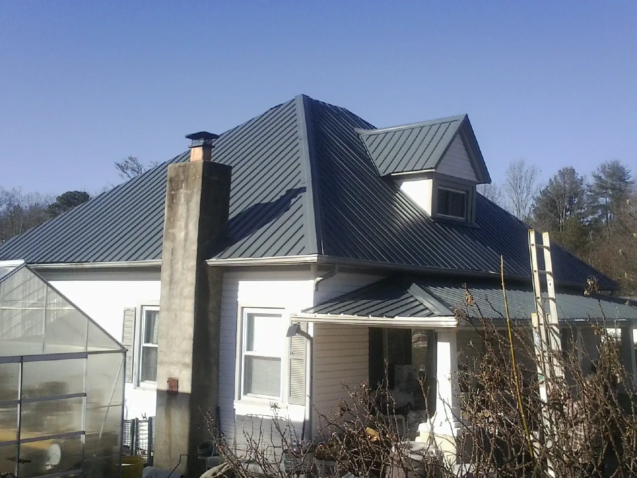 Dark blue standing seam metal roof on a white farmhouse with dormer in College Grove