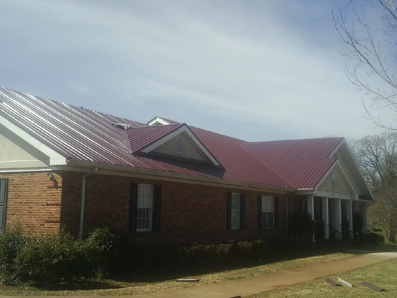 Red metal roof with gabled entries on a long brick building, from a Hail Damage Roof Repair job in College Grove