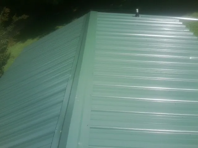 New green metal panels meeting at the ridge of a roof — Flat Roof Repair work by our crew in College Grove