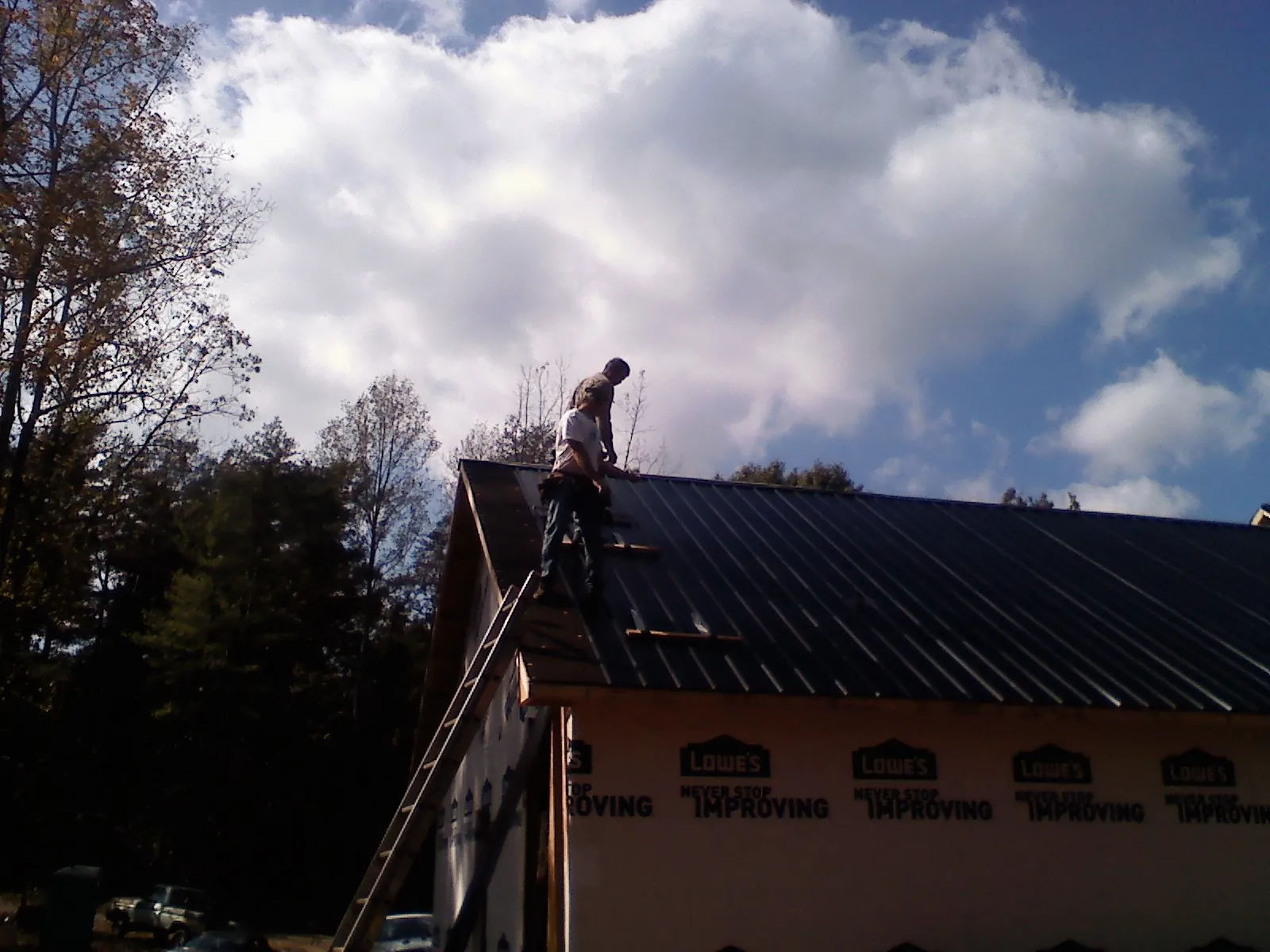 Roofer fastening dark metal panels high against a cloudy sky, from a Roof Inspection job in College Grove