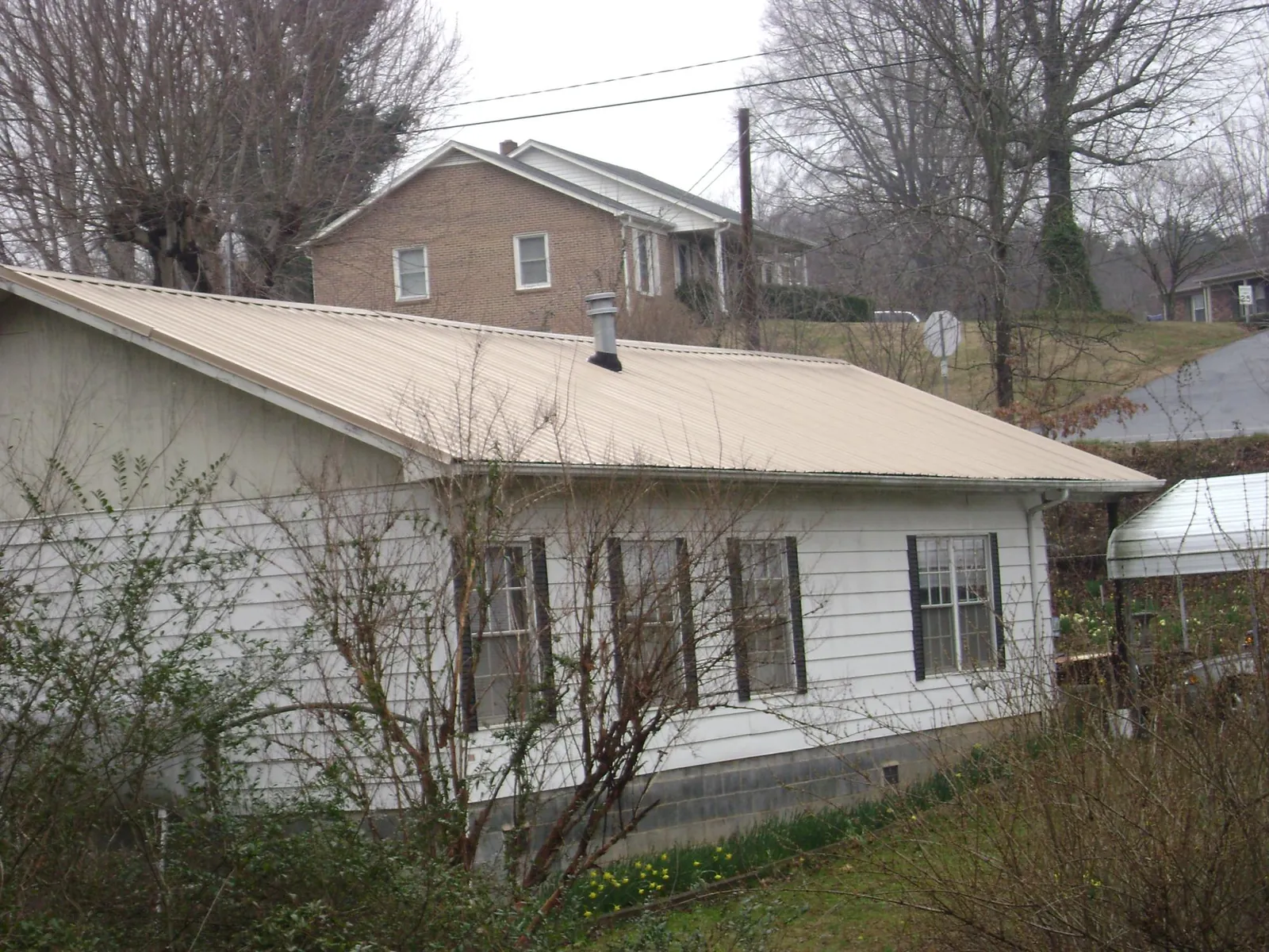Tan metal roof on a white sided house set into a hillside — Commercial Roofing by Roofing Brothers in College Grove