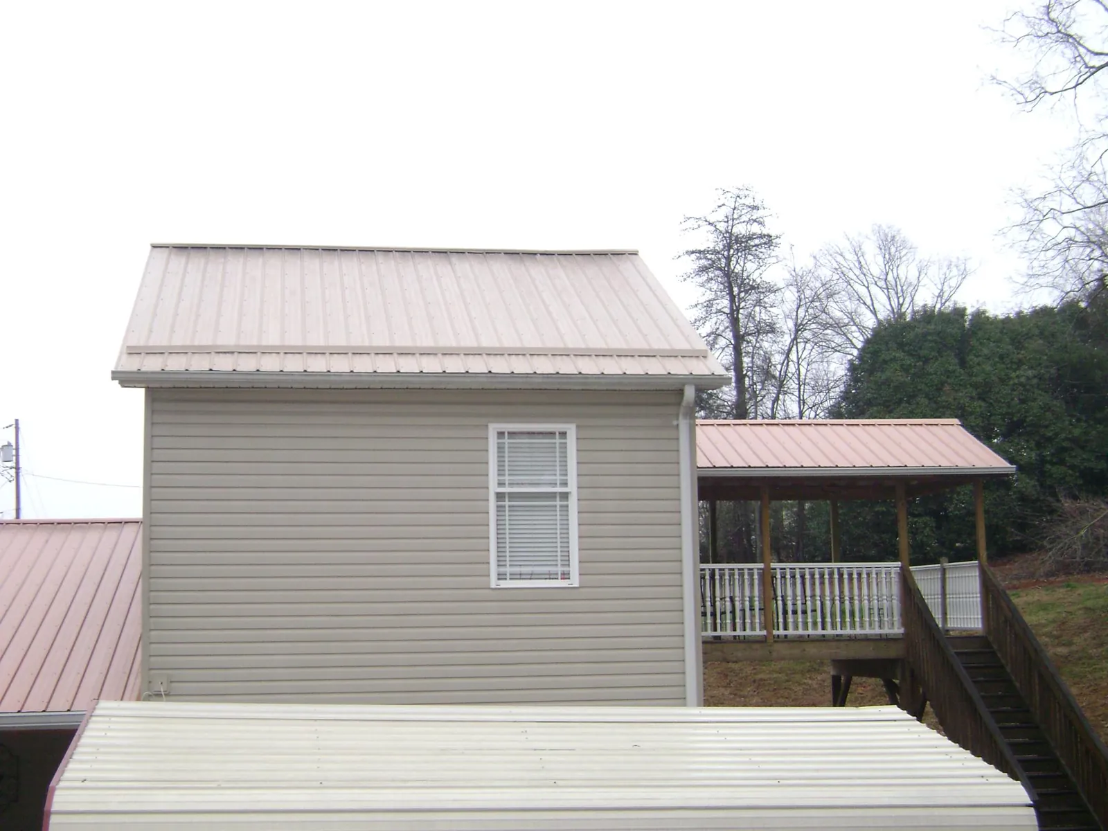 Tan metal roofs on a two story addition and attached porch, from a Roof Replacement job in College Grove